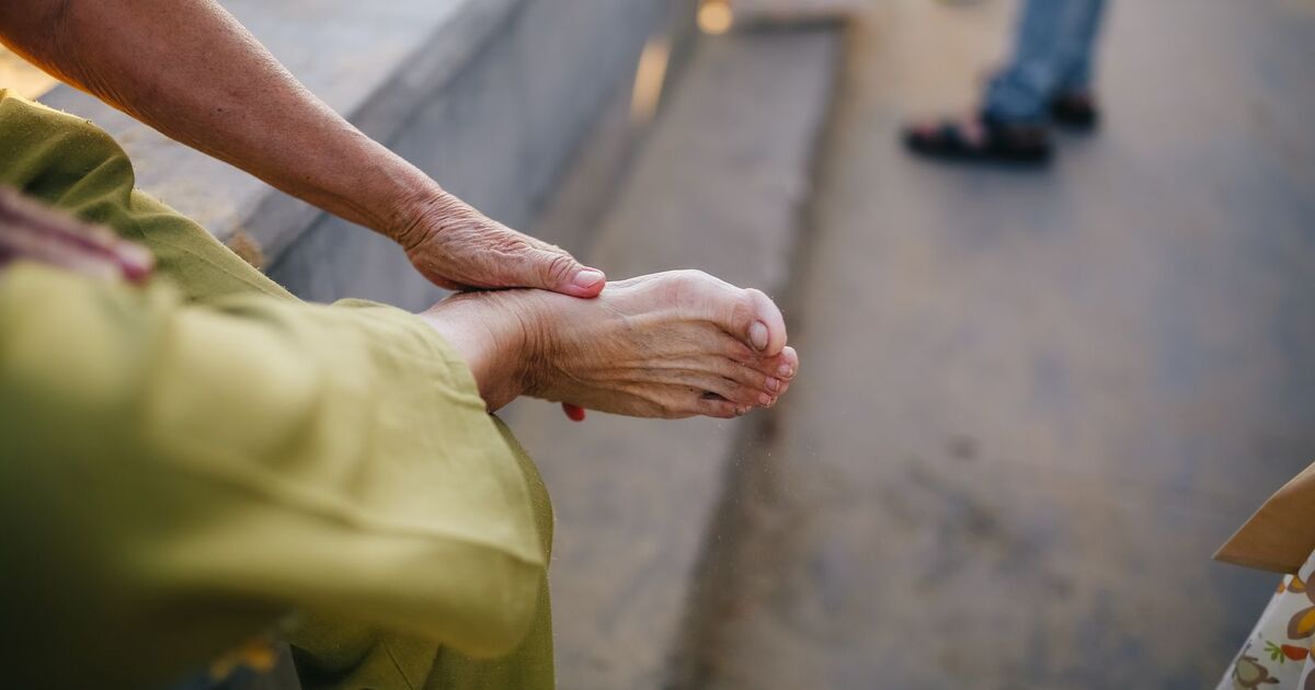Personne mature assise en extérieur, en train de masser doucement son pied pour soulager une articulation
