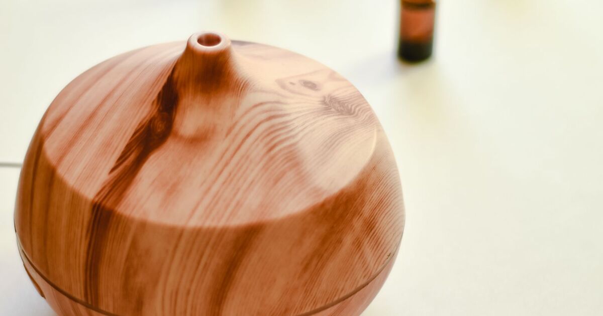 Diffuseur en bois et flacons d'huiles essentielles posés sur une surface claire, dans une ambiance feutrée