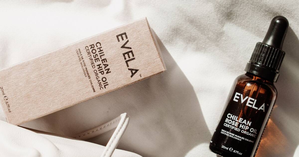 Flacon d'huile végétale rose élégamment posé sur un linge blanc texturé, lumière douce